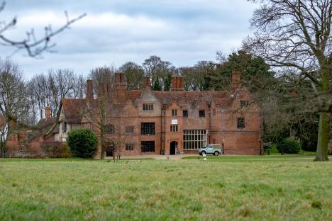 Spains Hall, a brick manor house, with a light green Land Rover parked in front.