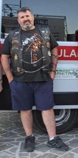Man in motorcycle vest standing in front of an ambulance.