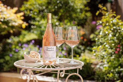 Bottle of Breath of Paradise rosé wine on a table outdoors with two glasses of wine and pistachios.