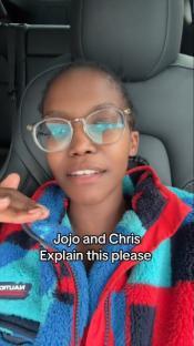 A person wearing glasses asks JoJo Siwa and Chris Hughes to explain something.