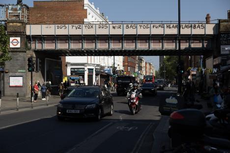 Street scene in Shepherd's Bush, London, under a graffiti-covered railway bridge.
