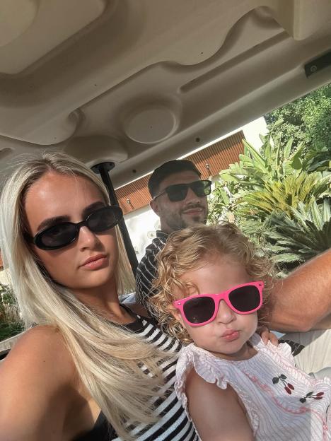 Molly Mae, a man, and a toddler in sunglasses riding in a golf cart.