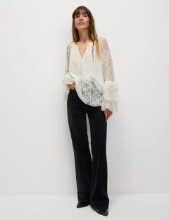 Woman wearing a white lace blouse and black flared jeans.
