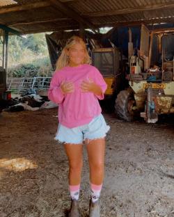Woman in pink sweater and denim shorts standing in a barn.