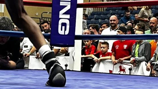 Boxer's legs and feet in a boxing ring with spectators watching.
