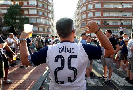 A Bilbao soccer fan with number 25 on his jersey holds a beer and gestures with his other arm.