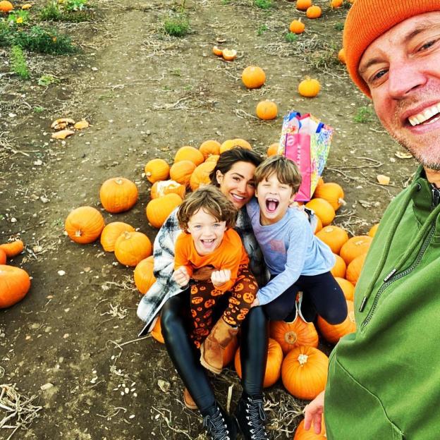 Frankie Bridge, her husband, and two children pose with pumpkins in a pumpkin patch.