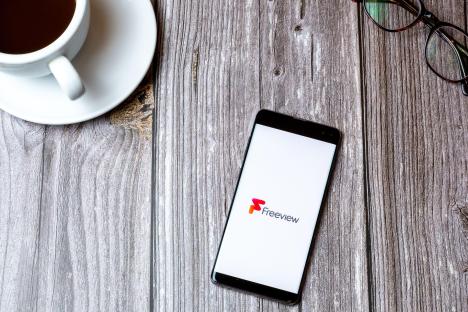 Smartphone displaying the Freeview app on a wooden table next to a cup of coffee and eyeglasses.