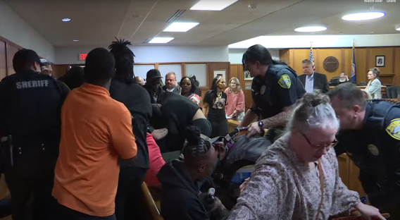 Chaos in a courtroom as law enforcement officers restrain individuals.