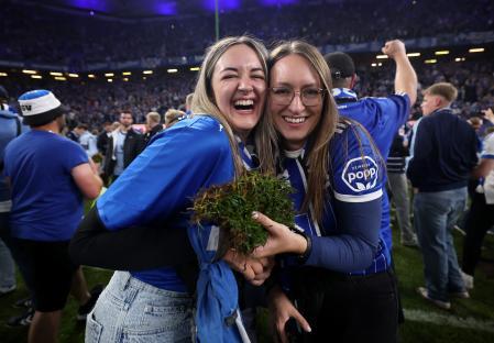 Two smiling women, wearing Hamburger SV jerseys, hold a clump of turf after a soccer match.