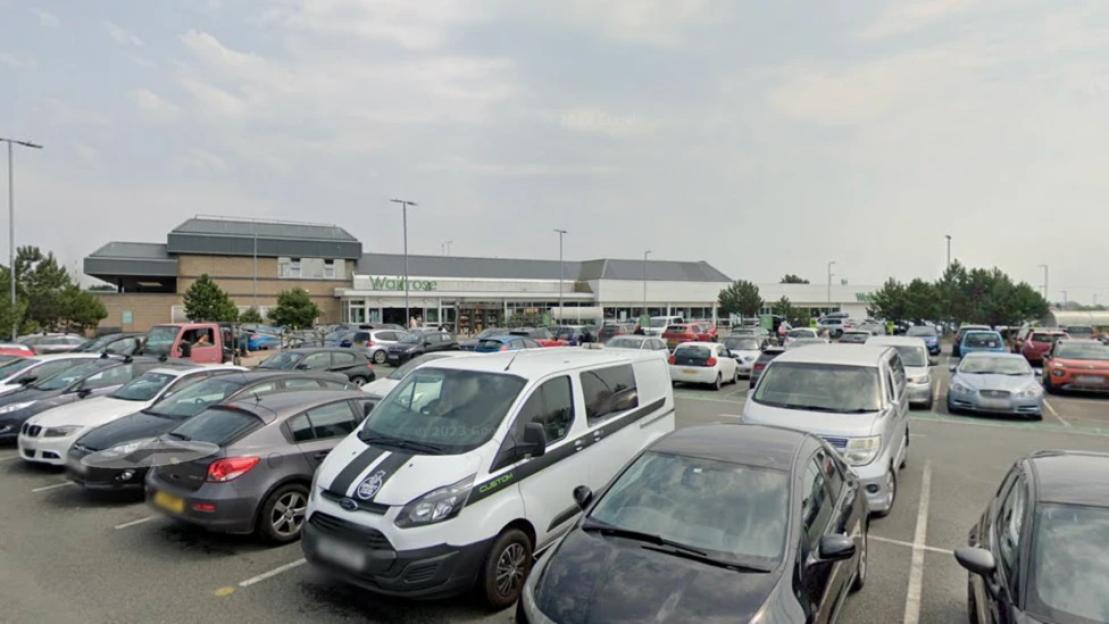 The exterior of a Waitrose supermarket from a busy parking lot.