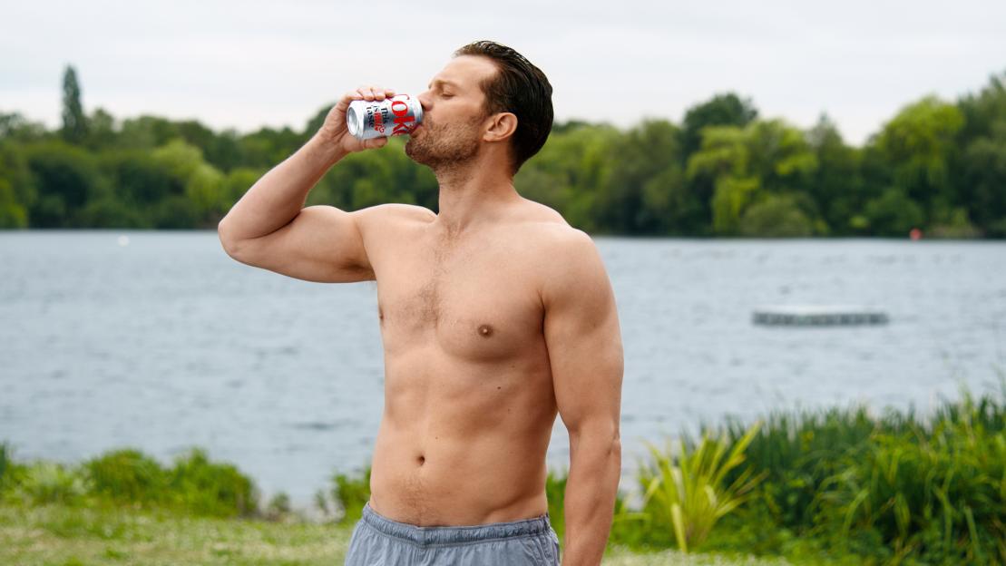 Jamie Dornan drinking Diet Coke by a lake.