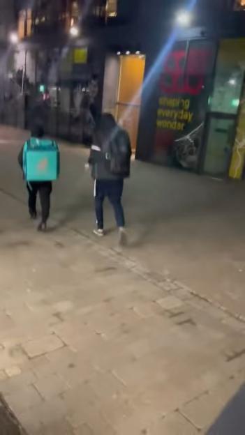 Two people walking away from a store at night, one wearing a teal delivery bag.