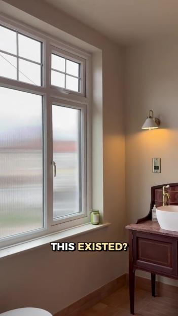 A bathroom with a large window covered in privacy film, a sink on a dark wood vanity, and a wall sconce.