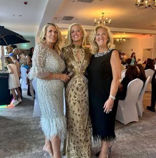 Three women in formal dresses at a wedding reception.