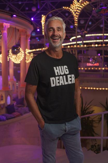Man in a "Hug Dealer" t-shirt smiling in a nightclub.