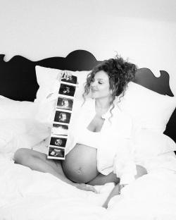 Black and white photo of a pregnant woman holding ultrasound images.