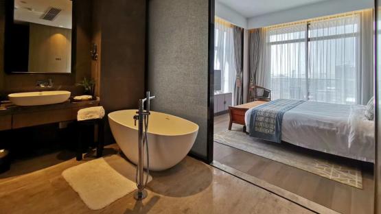 Hotel bathroom and bedroom with a freestanding bathtub and a bed.