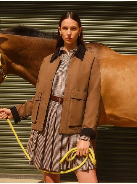 Woman in brown jacket and plaid skirt holding a horse's reins.