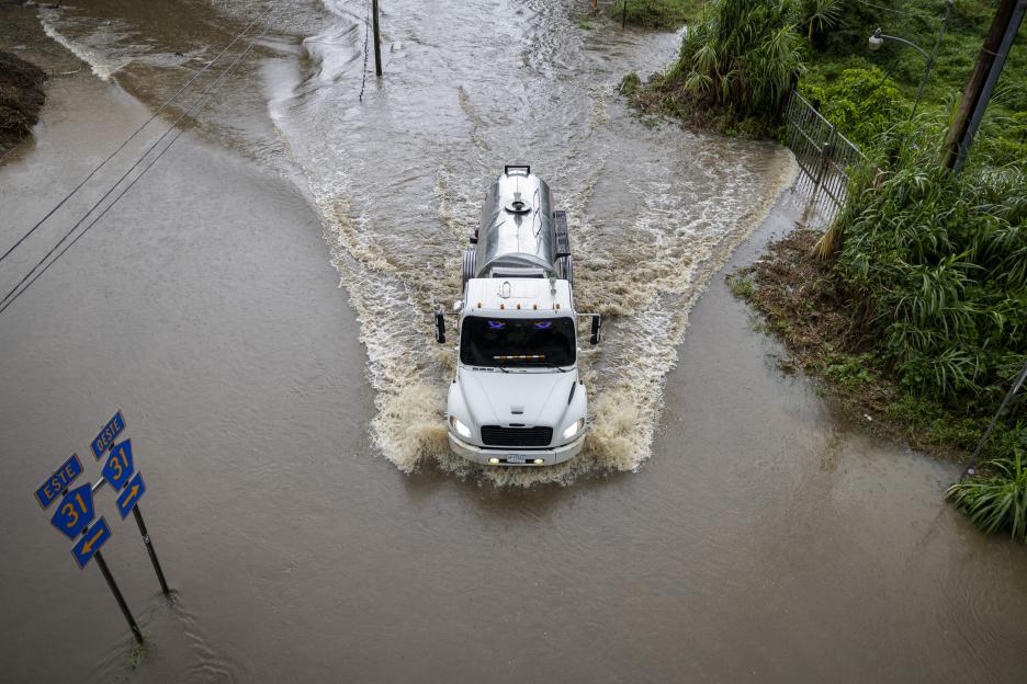 Truck driving through floodwaters on a road.