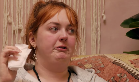 Screenshot of a young woman wiping her face with a tissue.