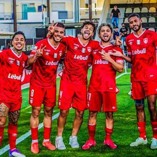 Five soccer players in red uniforms posing together.