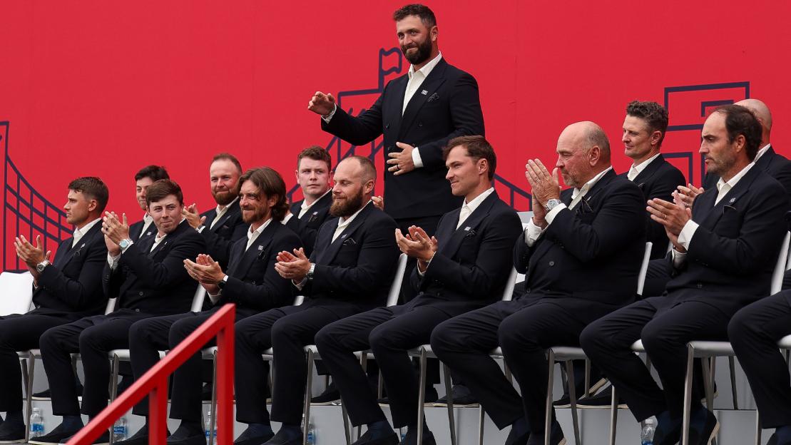 Jon Rahm standing while his Ryder Cup teammates sit and clap.