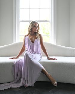 Amanda Holden in a lavender gown sitting on a white couch.