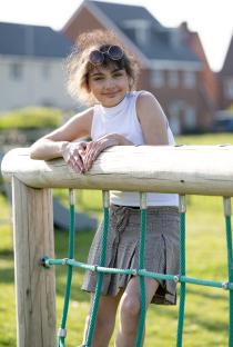Girl leaning on climbing frame, smiling.