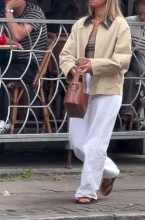 Woman walking down the street wearing white pants and a beige jacket.