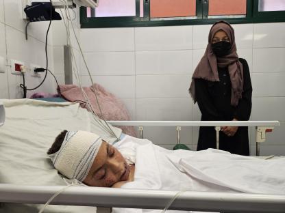 A wounded Palestinian child lies in a hospital bed, with a woman standing nearby.
