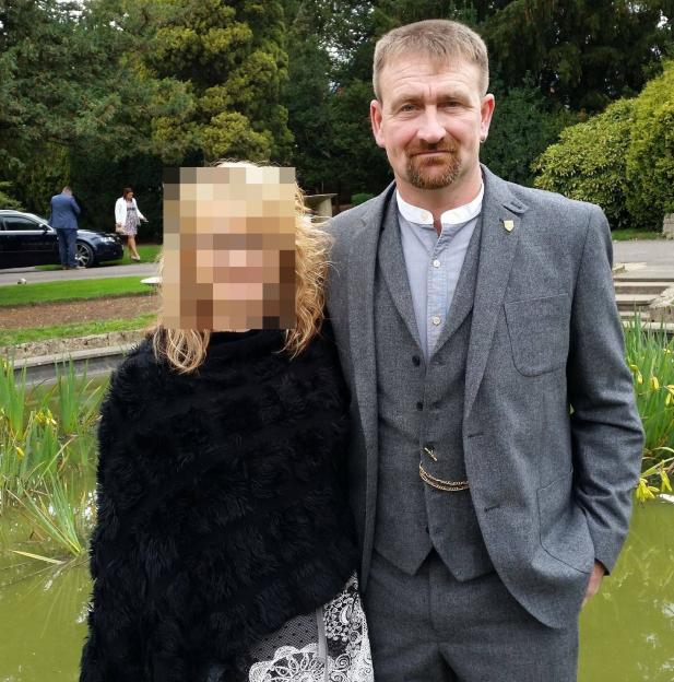 Photo of a man in a suit with a woman whose face is blurred.