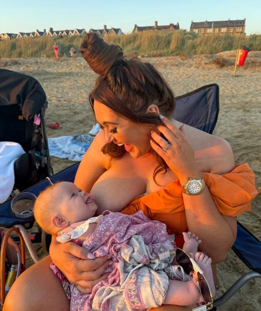 Woman breastfeeding baby on beach.
