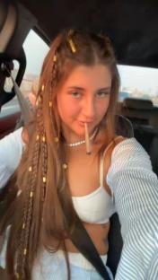 Selfie of a young woman with long braids and gold hair beads, holding a joint.