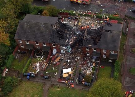 Aerial view of a house destroyed by an explosion, with emergency responders at the scene.