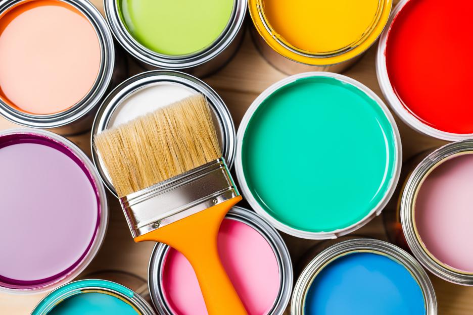 Top-down view of a paintbrush resting on open paint cans of various colors.