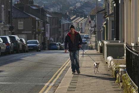 A man walks his dog down a residential street.