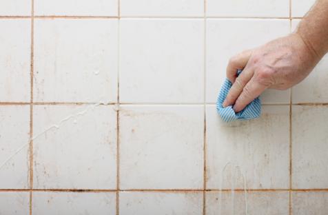 Hand cleaning dirty bathroom tiles with a cloth.