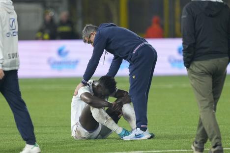 A dejected soccer player sits on the field while his coach comforts him.