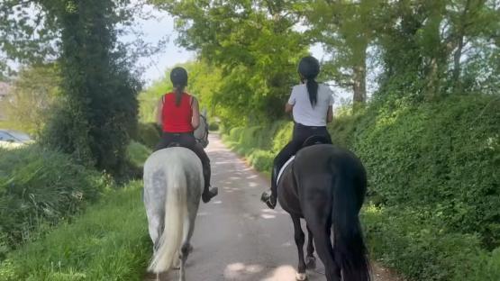 Two women horseback riding down a country lane.