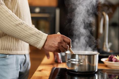 Close-up of a person's hands stirring a pot of steaming food on a stove.