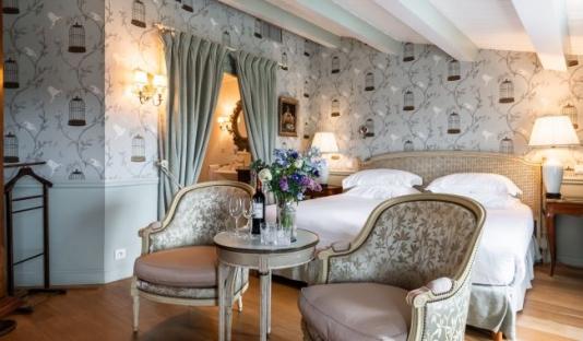 Hotel room with a bed, two armchairs, and a table with wine and flowers.