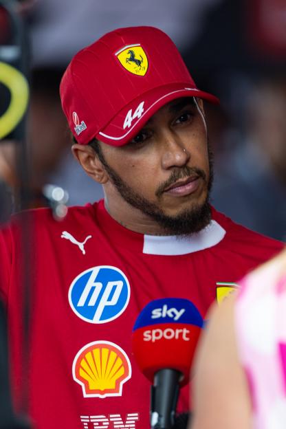 Lewis Hamilton in a Ferrari-branded shirt and cap, speaking into a microphone.
