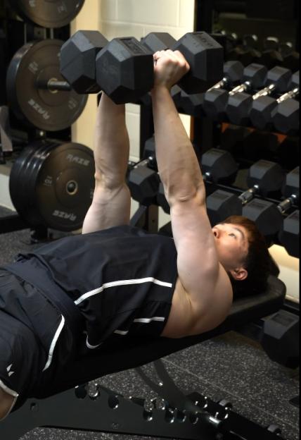 A person in a gym performing a dumbbell chest press.