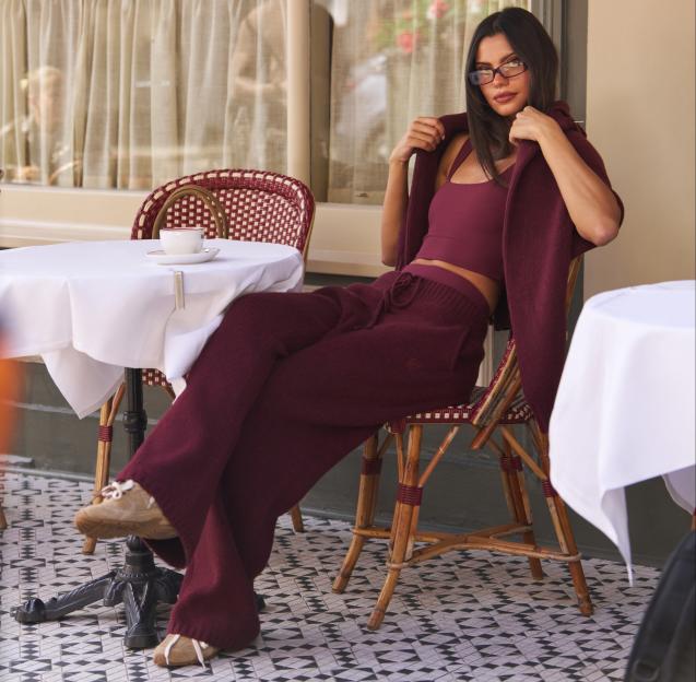 A woman in a burgundy loungewear set and glasses sits at a cafe table.