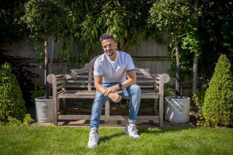 Peter Andre sitting on a wooden bench in his garden.