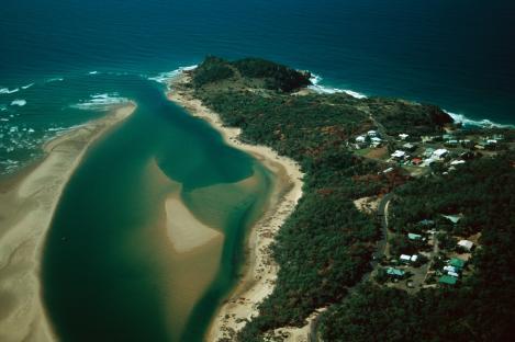Aerial view of Round Hill Head, showing a river inlet meeting the ocean, with a small town on the coast.