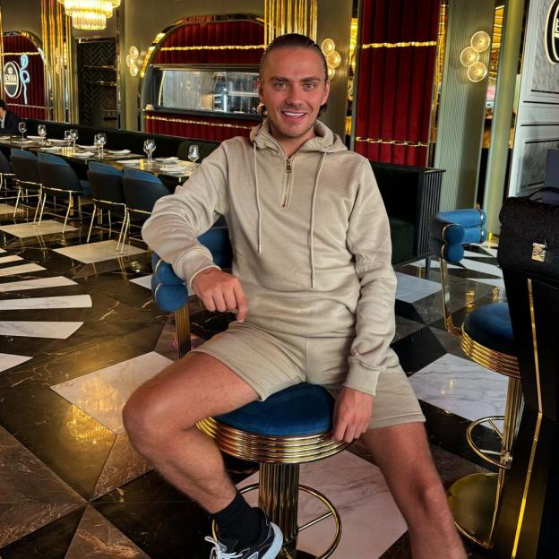 Man in beige shorts and sweatshirt sitting on a bar stool in a restaurant.