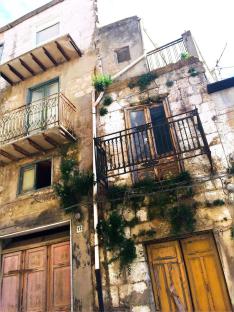 Distressed multi-story building with balconies and overgrown vegetation.