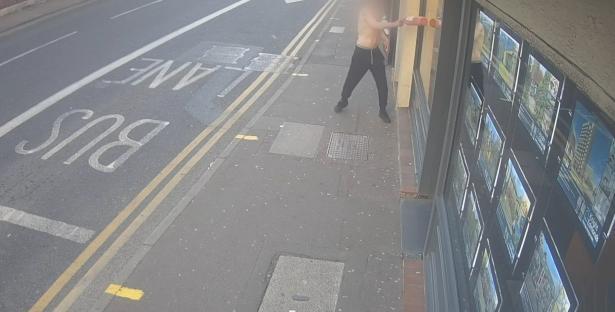 CCTV image of a man smashing shop windows with a fire extinguisher.